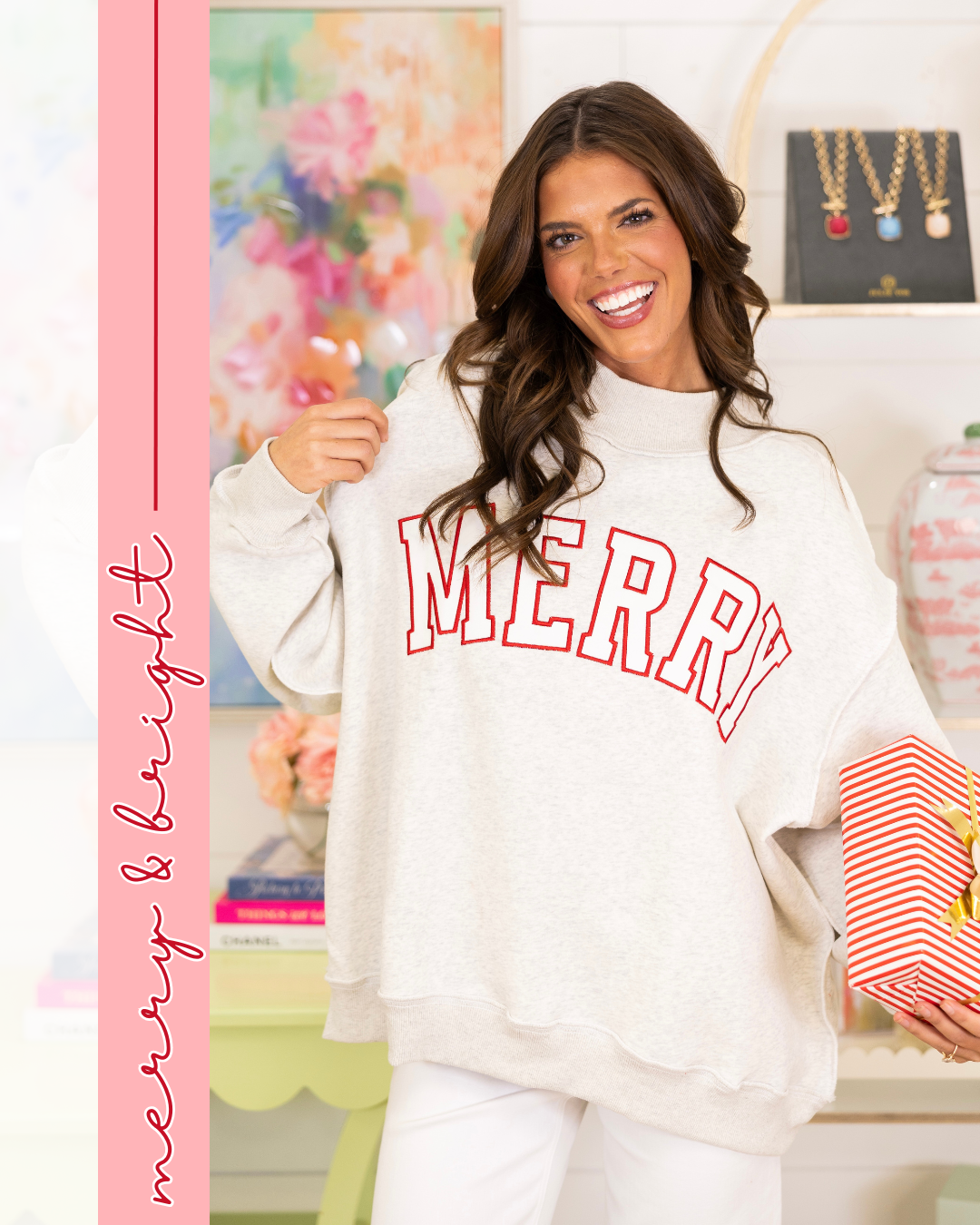 Woman smiling and holding a red-and-white striped gift box while wearing a cozy oversized light beige sweatshirt with bold red ‘MERRY’ lettering. The background features a chic boutique setting with jewelry and floral decor, and a vertical pink banner on the left reads ‘merry & bright’ in cursive.